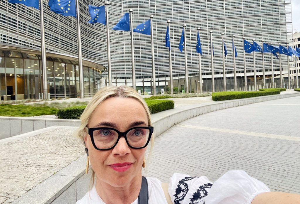 Terhi Tamminen ottaa selfien Brysselissä, taustalla liehuu monta EU:n lippua.