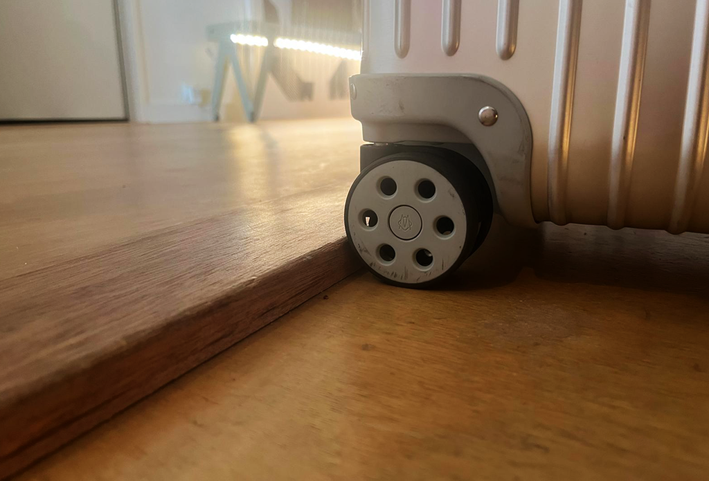 Matkalaukun pyörä jumissa puisen kynnyksen edessä.