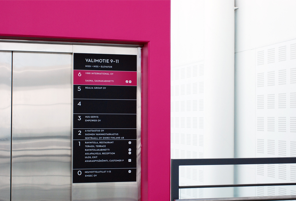 Seinän kirkas magenta väri saa hissin sekä tumman kerrosopasteen erottumaan vahvasti.